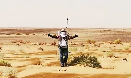 Surveyor carrying a GNSS receiver across desert terrain